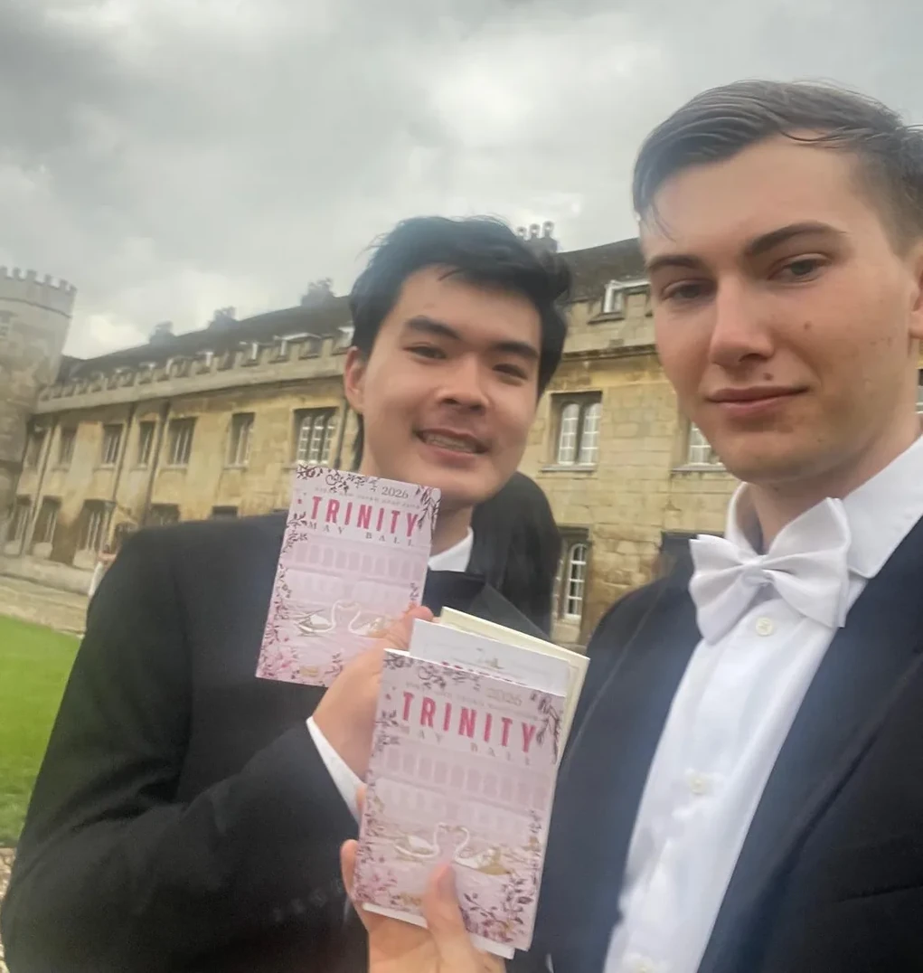 Atticus and a friend holding Trinity May Ball programs outdoors